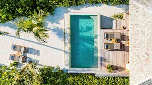 Ilmakuva uima-altaasta, ympäröivästä puisesta terassista, aurinkotuoleista ja kasveista. (Tekoälyn luoma teksti)