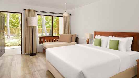 Hotellihuone, jossa on parivuode, istumapaikka ja ikkuna, joka avautuu vehreisiin puihin. (Tekoälyn luoma teksti)