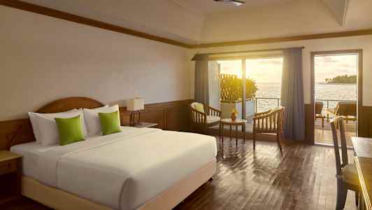 Hotellihuone, jossa on suuri sänky, kaksi nojatuolia ja pöytä, parveke merinäköalalla. (Tekoälyn luoma teksti)