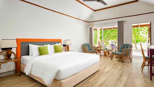 Huone, jossa on mukava parisänky, istuinryhmä tuoleineen ja pöytineen sekä suuret ikkunat, joista avautuu näkymä vehreään puutarhaan. (Tekoälyn luoma teksti)