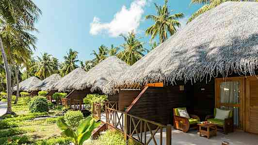 Kuvassa näkyy useita olkikattoisia bungaloweja trooppisten kasvien ja palmujen ympäröimänä. (Tekoälyn luoma teksti)