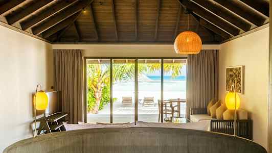 Huone, jossa kattopalkit ja näkymä rannalle suurten lasiovien kautta. (Tekoälyn luoma teksti)