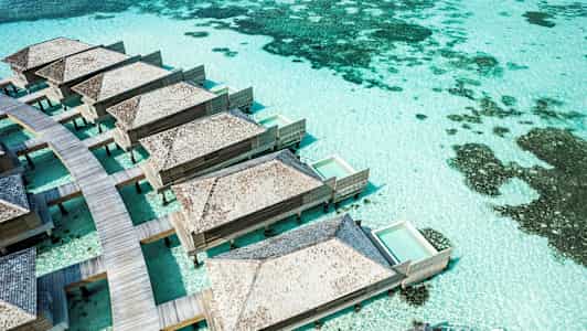 Paalujen päällä olevia bungaloweja yksityisillä uima-altailla turkoosin veden yläpuolella. (Tekoälyn luoma teksti)