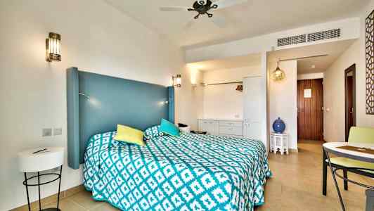 Hotellihuone, jossa on parivuode, sininen pääty, värikkäät tyynyt ja kuvioitu päiväpeite. Yksityiskohtiin kuuluu huonekaluja ja koristeellisia elementtejä. (Tekoälyn luoma teksti)