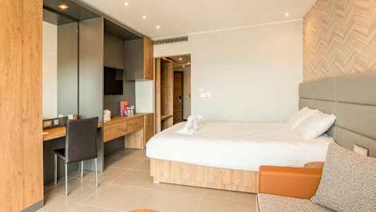 Hotellihuone, jossa on parivuode, kirjoituspöytä ja istuinalue. (Tekoälyn luoma teksti)