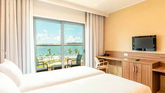 Hotellihuone, jossa kaksi vuodetta ja näkymä merelle lasioven kautta. (Tekoälyn luoma teksti)