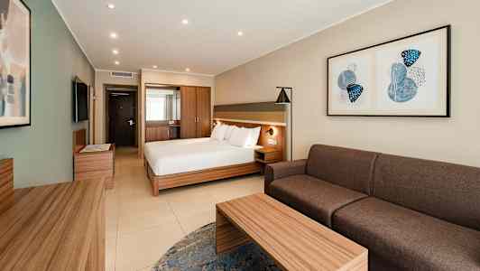 Hotellihuone, jossa on parivuode, sohva, pöytä ja seinätaidetta. (Tekoälyn luoma teksti)