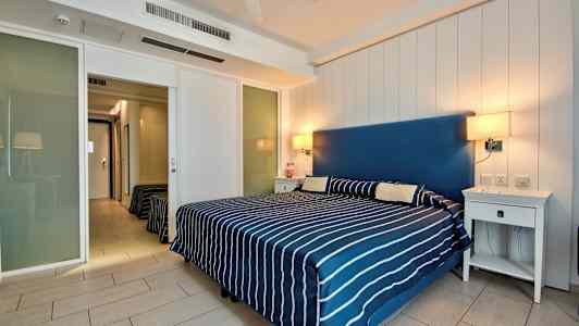 Makuuhuone, jossa on parivuode raidallisella peitteellä ja kaksi yöpöytää. (Tekoälyn luoma teksti)