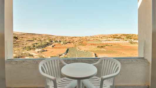 Kaksi valkoista muovista tuolia ja pyöreä pöytä terassilla, näkymä viljelysmaalle. (Tekoälyn luoma teksti)