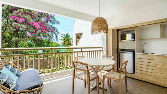 Terassi, jossa pöytä ja tuolit, sekä näkymä vehreyteen ja kukkiin. (Tekoälyn luoma teksti)