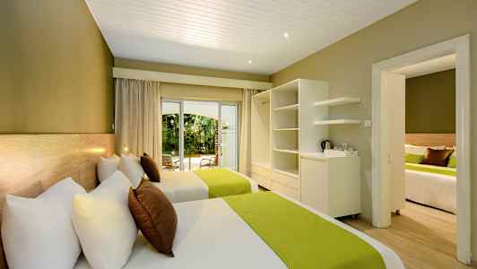 Hotellihuone, jossa on kaksi vuodetta, vihreät päiväpeitteet ja näkymä puutarhaan. (Tekoälyn luoma teksti)