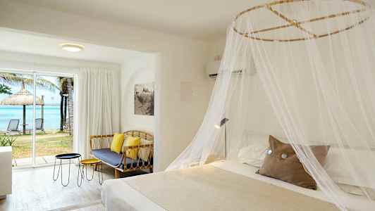 Hotellihuone, jossa suuri hyttysverkolla peitetty sänky, sohva, pöydät ja suuri ikkuna, josta on näkymä rannalle ja merelle. (Tekoälyn luoma teksti)