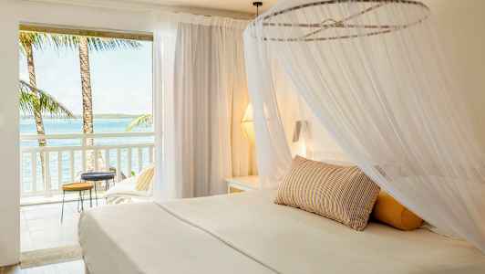 Vaalea hotellisviitti, jossa on pylvässänky ja näkymä merelle parvekkeelta. (Tekoälyn luoma teksti)