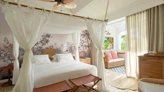 Makuuhuone, jossa on pylvässänky, seinäkoriste ja sisustus vaaleilla huonekaluilla sekä istuinryhmä ikkunan äärellä. (Tekoälyn luoma teksti)