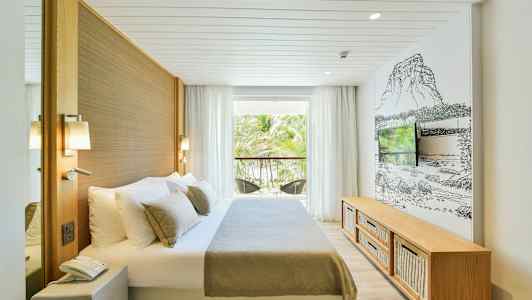 Hotellihuone, jossa on sänky, televisio ja parveke, josta on näkymä palmupuille. (Tekoälyn luoma teksti)