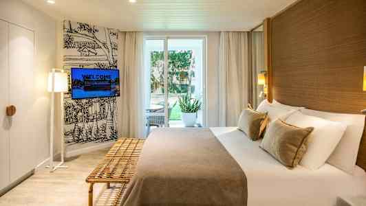 Hotellihuone, jossa parivuode, ulkoistuimet oven vieressä ja seinälle asennettu televisio. (Tekoälyn luoma teksti)