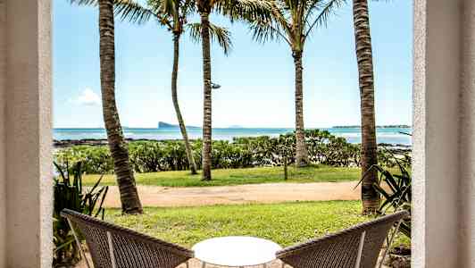 Kaksi tuolia ja pöytä, näkymä merelle palmujen läpi. (Tekoälyn luoma teksti)