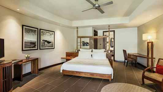 Nykyaikaisesti sisustettu hotellihuone, jossa on parivuode, kirjoituspöytä ja tuoli, seinätaidetta ja kattotuuletin. (Tekoälyn luoma teksti)