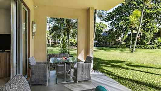 Näkymä terassilta, jossa puutarhakalusteita, kohti vehreää aluetta ja palmuja. (Tekoälyn luoma teksti)