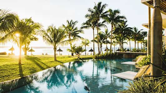 Näkymä altaalle, jossa aurinkotuoleja, palmuja ja näkymä rannalle meren äärellä. (Tekoälyn luoma teksti)