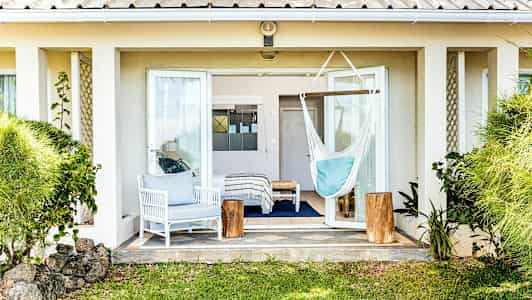 Kuva terassista, jossa on avoin terassiovi, valkoinen istuinryhmä, riippumatto ja vihreitä kasveja ympärillä. (Tekoälyn luoma teksti)