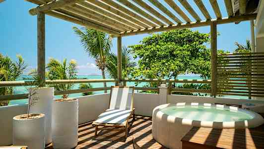 Puisella terassilla on aurinkotuoli, kolme valkoista kukkaruukkua ja poreallas, näkymä merelle ja ympäröiville palmuiille. (Tekoälyn luoma teksti)