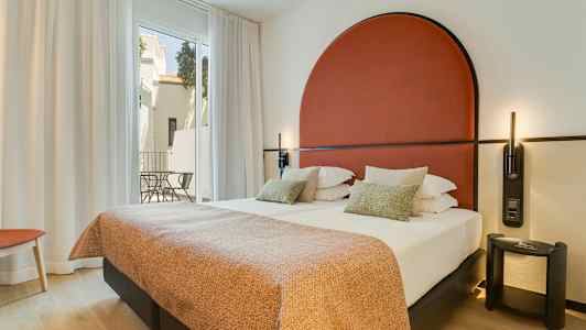 Moderni hotellihuone, jossa parivuode, punainen pääty ja suuret ikkunat parvekkeelle. (Tekoälyn luoma teksti)