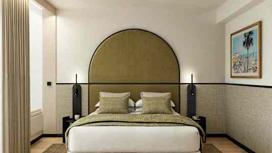 Hotellihuone, jossa on sänky, vihreitä tyynyjä ja kehystetty taulu seinällä. (Tekoälyn luoma teksti)