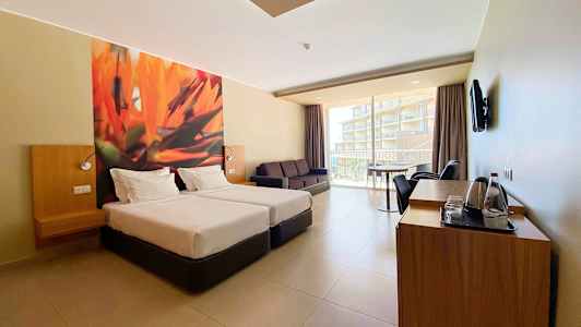 Hotellihuone, jossa kaksi yhden hengen vuodetta, sohva ja parveke näkymällä. (Tekoälyn luoma teksti)