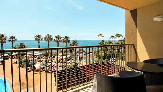 Näköala parvekkeelta, jossa on huonekalut, uima-allasalueelle, palmuja ja meri taustalla. (Tekoälyn luoma teksti)