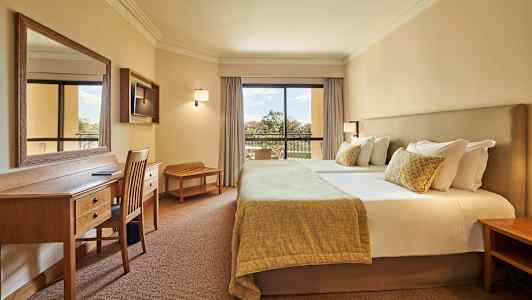 Kuva hotellihuoneesta, jossa on parivuode, työpöytä ja tuoleja sekä parveke näkymällä. (Tekoälyn luoma teksti)