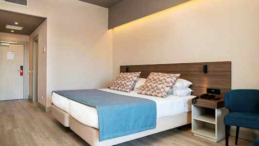 Hotellihuone, jossa on parivuode, sininen huopa ja tyynyjä, vieressä tuoli ja yöpöytä. (Tekoälyn luoma teksti)