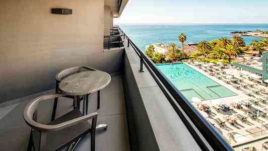 Parveke, jossa pöytä ja tuolit, näkymä uima-altaalle ja merelle. (Tekoälyn luoma teksti)