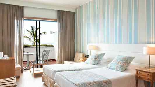 Hotellihuone, jossa kaksi erillistä vuodetta, koristeelliset tyynyt ja parveke, varustettuna tuoleilla ja pöydällä. (Tekoälyn luoma teksti)