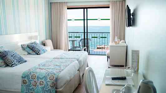 Hotellihuone, jossa on sänky, kirjoituspöytä ja näkymä merelle parvekkeelta. (Tekoälyn luoma teksti)