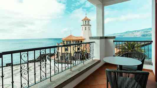 Näkymä parvekkeelta merelle, etualalla majakka ja rakennuksia. (Tekoälyn luoma teksti)