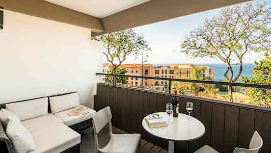 Terassi, jossa on istuinryhmä ja näkymä merelle, pöytä ja kaksi viinilasia. (Tekoälyn luoma teksti)