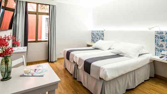 Hotellihuone, jossa kaksi sänkyä, pöytä koristeellisella vaasilla ja ikkuna. (Tekoälyn luoma teksti)