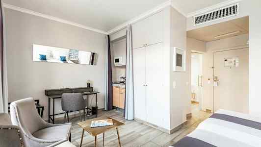 Huone, jossa on istuimet, kirjoituspöytä, sänky ja keittonurkkaus. (Tekoälyn luoma teksti)