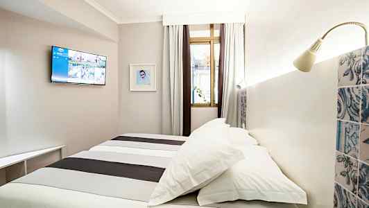 Hotellihuone, jossa on sänky, seinään kiinnitetty televisio ja ikkunat verhoilla. (Tekoälyn luoma teksti)