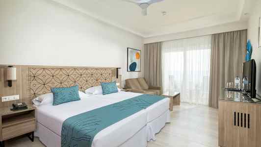 Kuva hotellihuoneesta, jossa on parisänky, istuinalue ja parveke. (Tekoälyn luoma teksti)