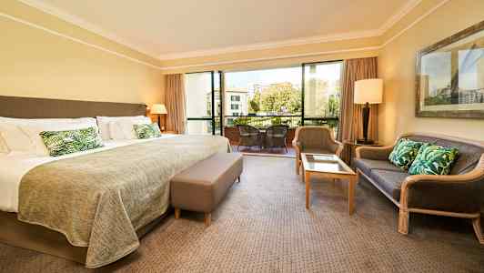 Hotellihuone, jossa suuri sänky, istuinalue ja parveke näkymillä. (Tekoälyn luoma teksti)