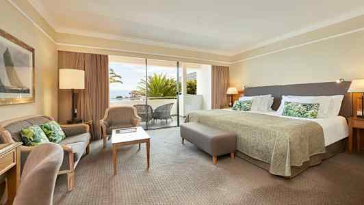 Hotellihuone, jossa on suuri vuode, istuinryhmä ja parveke näkymällä. (Tekoälyn luoma teksti)