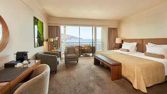 Hotellihuone, jossa on parivuode, istuinryhmä ja parveke merinäköalalla. (Tekoälyn luoma teksti)