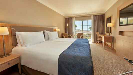 Hotellihuone, jossa on kaksi erillistä vuodetta ja parveke näkymällä. (Tekoälyn luoma teksti)