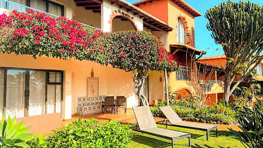 Rakennus kukkakoristeilla, viheralueilla ja aurinkotuoleilla nurmikolla. (Tekoälyn luoma teksti)