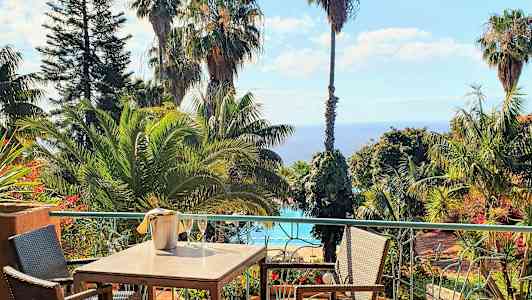 Ruokapöytä terassilla, jolta on näkymä trooppisiin puihin, uima-altaalle ja merelle. (Tekoälyn luoma teksti)