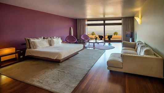 Modernisti sisustettu hotellihuone, jossa on parivuode, sohva, istuinryhmä ja suuret ikkunat näkymällä. (Tekoälyn luoma teksti)