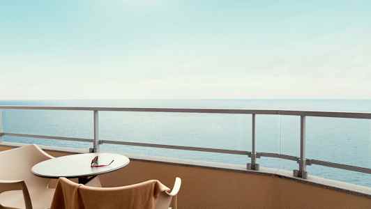 Näkymä parvekkeelta, jossa on pöytä, tuolit ja lasikaide, taustalla näkyy meri. (Tekoälyn luoma teksti)