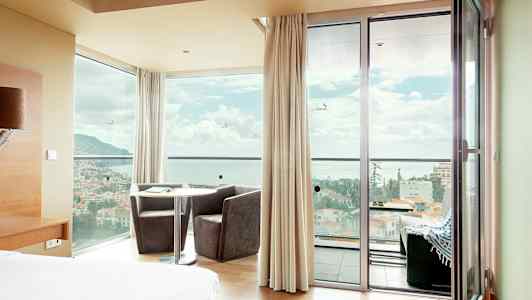 Hotellihuone, josta on panoraamanäkymä ikkunoiden ja ovien läpi kaupunkiin meren edustalla. (Tekoälyn luoma teksti)